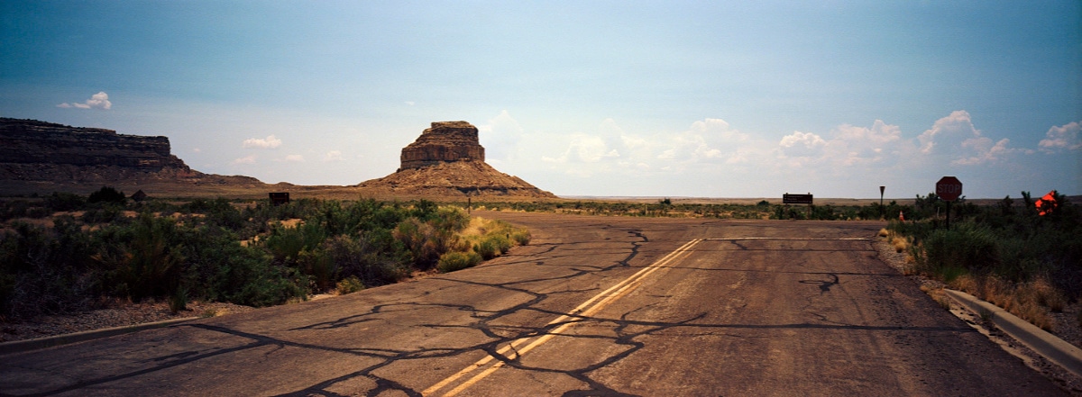 Cracked road with tall rock formations in the background in Chaco Canyon, New Mexico, USA. Taken by Lucas Taylor on a Hasselblad XPan camera.